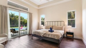 Een slaapkamer met een bed, een nachtkastje, een stoel, een raam en uitzicht op een zwembad.