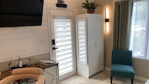 A modern living room with a teal armchair, a white cabinet, a small table with a bottle and glasses, and a potted plant on a cabinet. - Ruscincy’s Rest "minutes drive to Orioles stadium" (Baltimore)