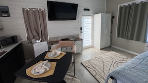 A compact living space with a dining table set for two, a flat-screen TV mounted on the wall, a kitchenette with a microwave, and a sliding door closet. - Ruscincy’s Rest "minutes drive to Orioles stadium" (Baltimore)
