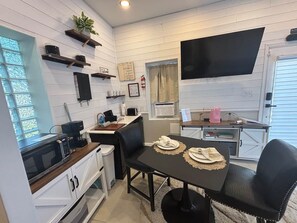 A compact kitchen with a microwave, coffee maker, and a dining area with a table and chairs. - Ruscincy’s Rest in Historic Arcadia-Beverly Hills (Baltimore)