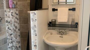 A bathroom with a white pedestal sink, a mirror above it, and a shower area with stone tiles.