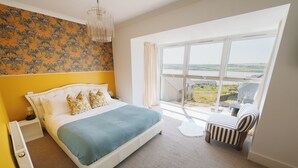 Ein Schlafzimmer mit einem großen Bett, Blick auf die Landschaft und einem gestreiften Sessel am Fenster.
