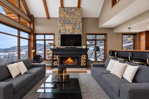 A modern living room with a stone fireplace, large windows, and a cozy seating area. - Tremblant Prestige - Altitude 170-9 (Mont-Tremblant)
