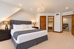 A bedroom with a large bed, two bedside tables, a chandelier, and a door leading to a bathroom. - Tremblant Prestige - Altitude 170-9 (Mont-Tremblant)