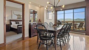A spacious dining area with a large table and chairs, a modern chandelier, and a view of the outdoors through large windows. - Tremblant Prestige - Altitude 170-9 (Mont-Tremblant)