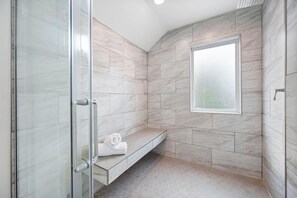 A modern bathroom with a glass shower enclosure, a bench with towels, and a large window. - Mavericks Penthouse – Downtown Luxury on Main Street, Half Moon Bay (Half Moon Bay)