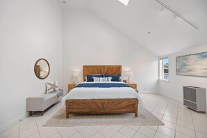 A bedroom with a wooden bed, a gray sofa, a round mirror, and a large window. - Mavericks Penthouse – Downtown Luxury on Main Street, Half Moon Bay (Half Moon Bay)