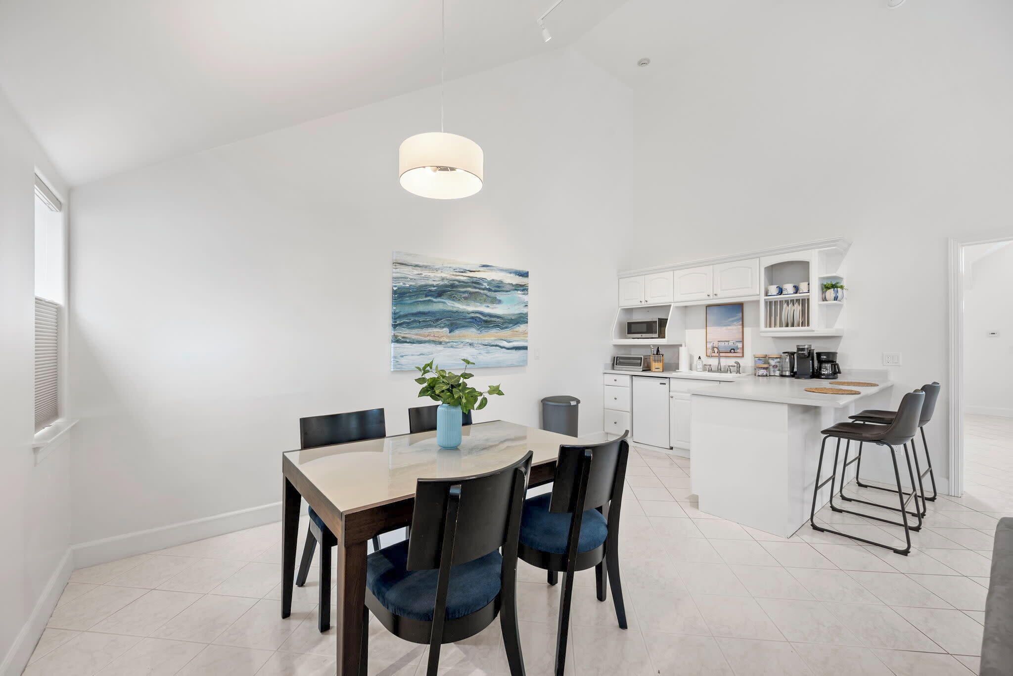 A modern kitchen with white cabinetry, a central island, and a dining area with a table and chairs.