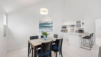 A modern kitchen with white cabinetry, a central island, and a dining area with a table and chairs.