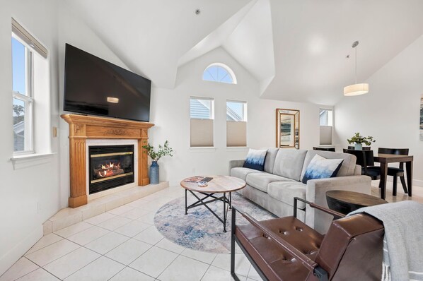 A spacious living room with a fireplace, a large TV, a sofa, and a dining area. - Mavericks Penthouse – Downtown Luxury on Main Street, Half Moon Bay (Half Moon Bay)