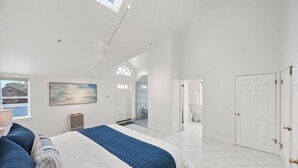 Un dormitorio amplio con una cama grande, un tragaluz, un cuadro y vistas al exterior.