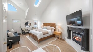 Un dormitorio espacioso con una cama grande, un televisor sobre la chimenea y un tragaluz.