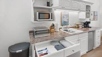 Una cocina moderna con armarios blancos, microondas, tostadora, fregadero y cafetera.