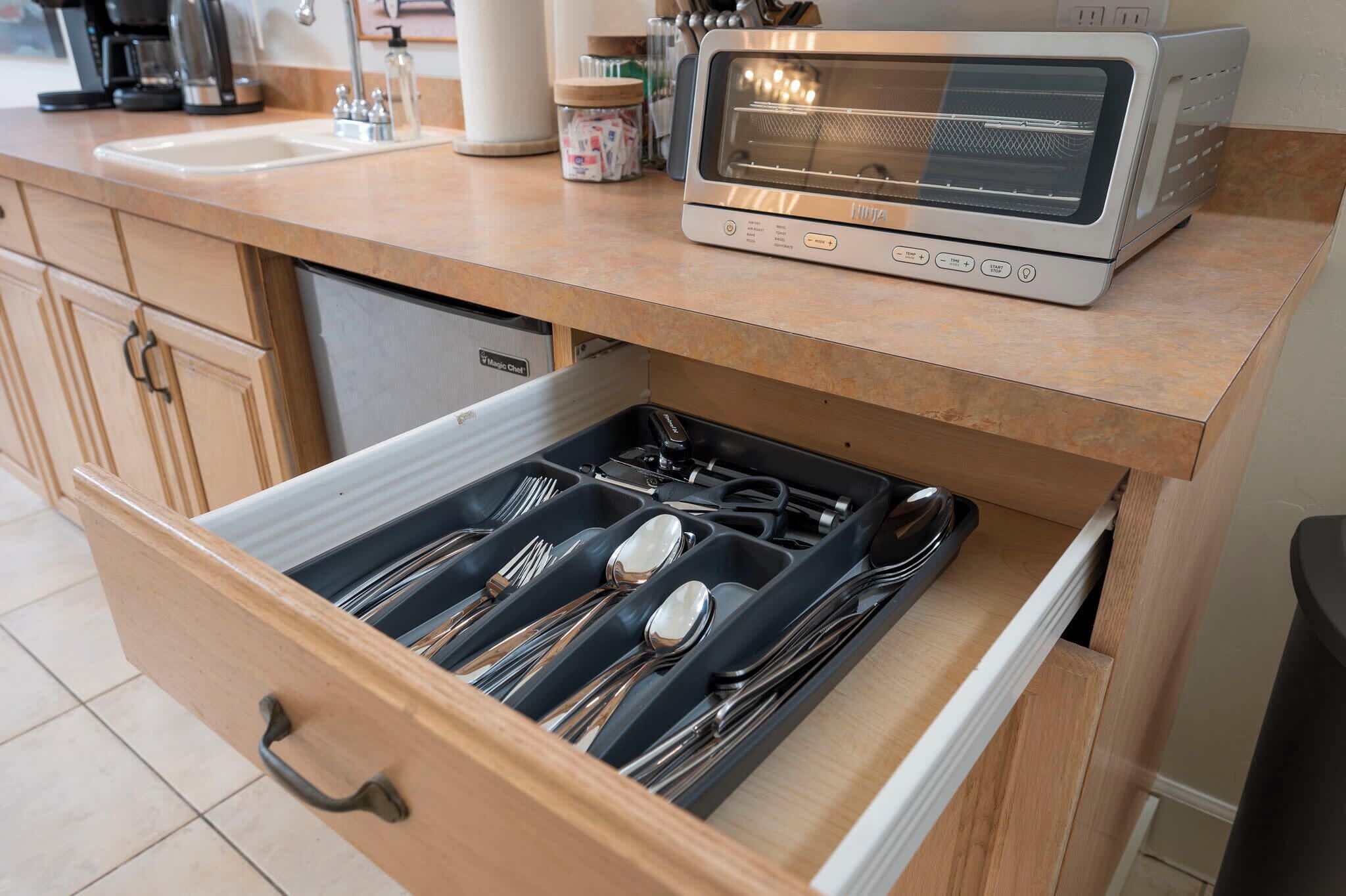 Una cocina con horno tostador en la encimera, un cajón con utensilios y una cafetera al fondo.