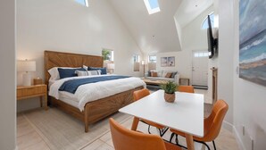 Un dormitorio moderno con una cama grande, una mesa de comedor, sillas naranjas y tragaluces.