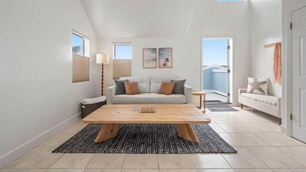 Un salón espacioso con una gran mesa de centro de madera, un sofá con cojines estampados y vistas al exterior a través de un ventanal.