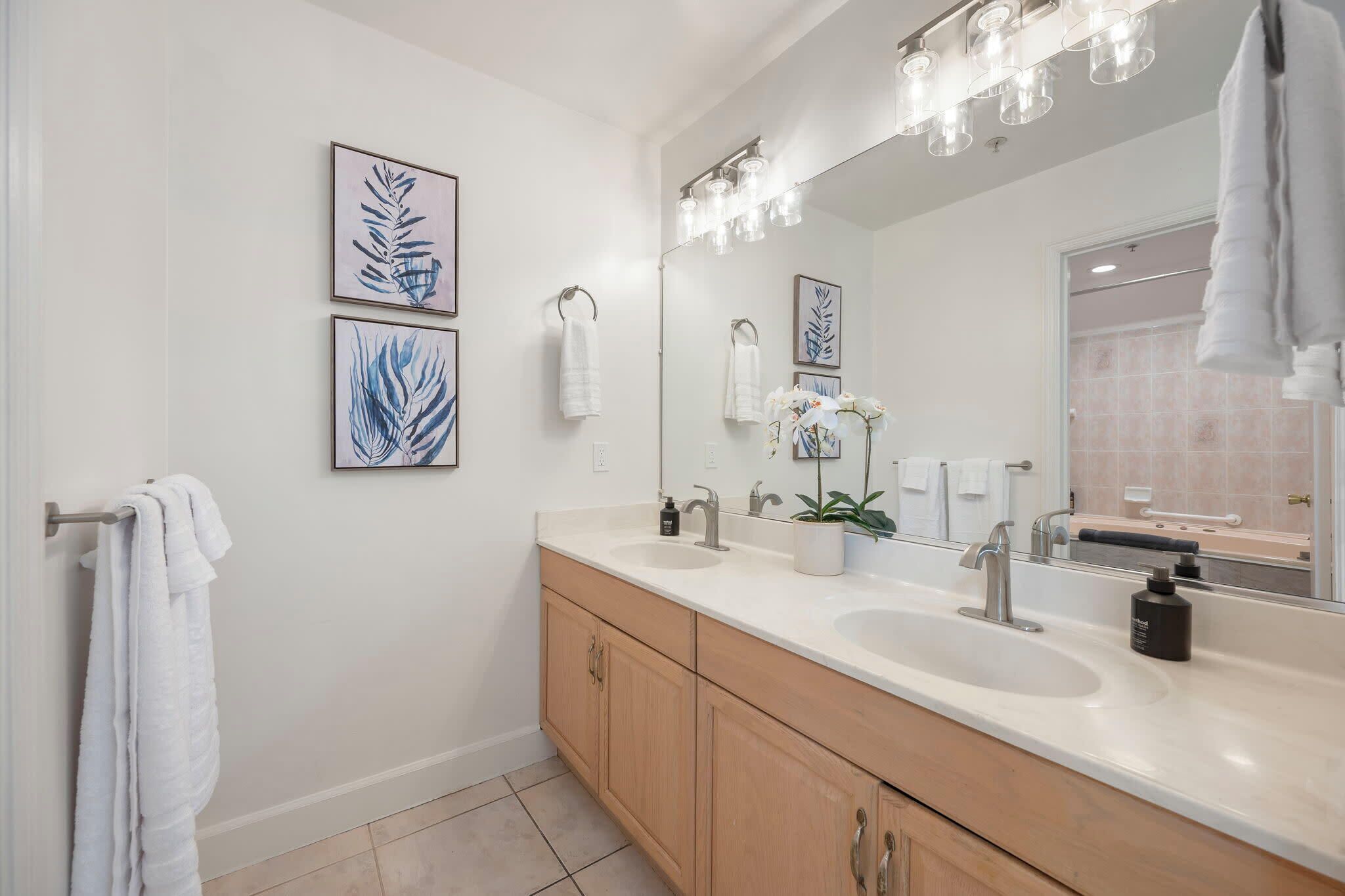 A modern bathroom with two sinks, a large mirror, and framed artwork on the wall.