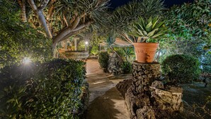 A nighttime garden pathway with a stone wall, potted plants, and a metal structure in the background. - Right in the center of Ischia, the ideal villa for comfortable exclusive vacations (Ischia)