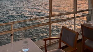 A table with a glass of water and a chair, overlooking a sunset over the ocean from a balcony with a railing. - Right in the center of Ischia, the ideal villa for comfortable exclusive vacations (Ischia)