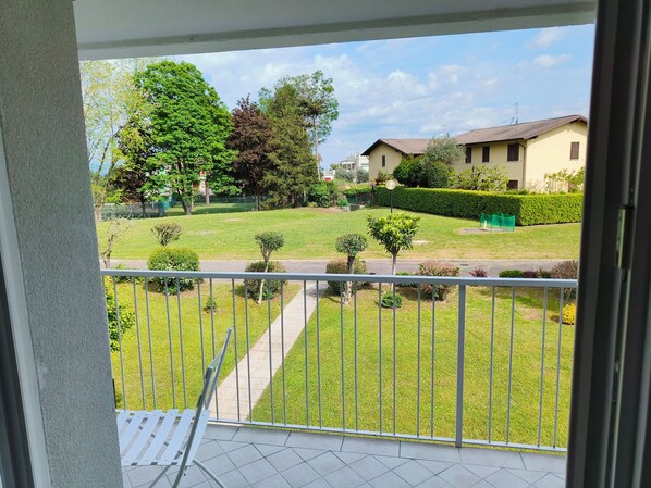 Een balkon met uitzicht op een verzorgd gazon, een haag en een gebouw op de achtergrond.