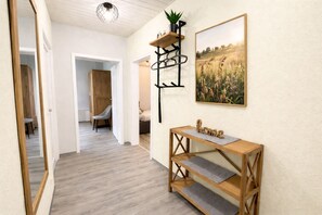 Un couloir avec une console en bois, un miroir, une plante en pot et un tableau représentant un paysage, encadré.