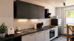 A modern kitchen with dark cabinets, a stainless steel sink, and a built-in oven. - Dessau UNESCO vacation apartment "Franz" - for nature and culture lovers (Dessau-Roßlau)