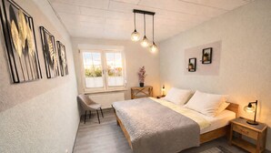 A bedroom with a bed, bedside tables, a chair, a window, and wall art. - Dessau UNESCO vacation apartment "Franz" - for nature and culture lovers (Dessau-Roßlau)