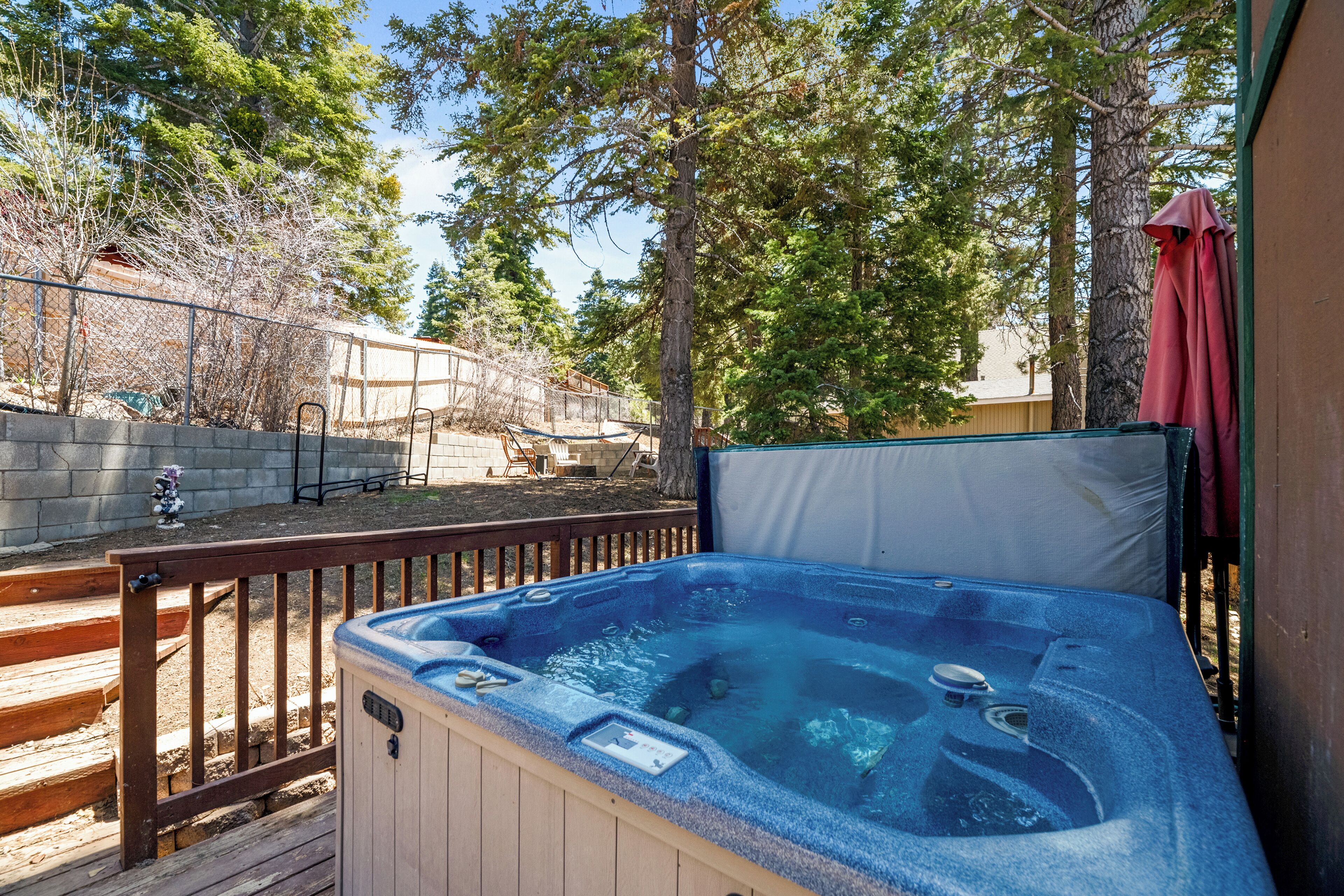 Un jacuzzi en una terraza de madera con valla de madera y árboles al fondo.