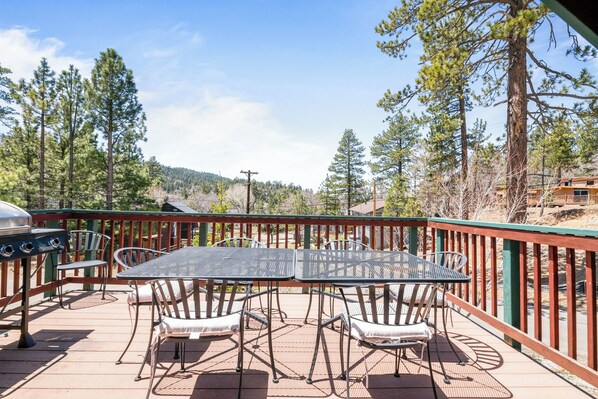 An outdoor patio with a metal table and chairs, surrounded by a wooden deck and a metal railing. - Buffalo Crossing (Big Bear Lake)