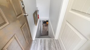A narrow hallway with a wooden floor, white walls, and a door on the left. - Beautiful Basement Private Suite Prime Location (Winnipeg)