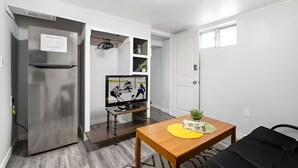 A compact living space with a kitchenette, a flat-screen TV, a wooden table, and a black sofa. - Beautiful Basement Private Suite Prime Location (Winnipeg)