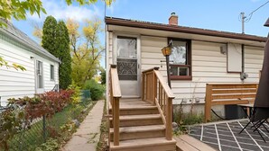 A residential property with a wooden staircase leading to a front door, a fenced garden, and a bench in the yard. - Beautiful Basement Private Suite Prime Location (Winnipeg)