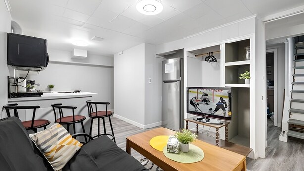 A modern living room with a sofa, a coffee table, a TV, a kitchen area, and a dining space. - Beautiful Basement Private Suite Prime Location (Winnipeg)
