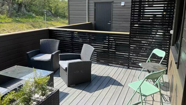 A deck with wicker furniture, a glass table, and a view of a building in the background.
