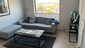 A modern living room with a grey sofa, a black coffee table, and a view of a green landscape through a large window.