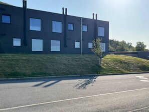 Un edificio moderno con techo plano, múltiples ventanas y un área verde al frente.