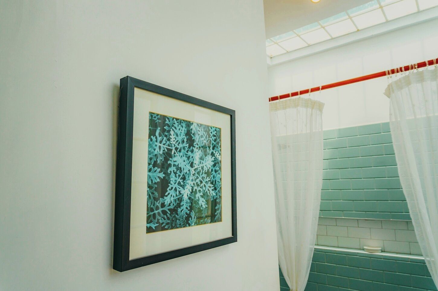 A framed artwork on a wall, a staircase with green tiles, and a white curtain.