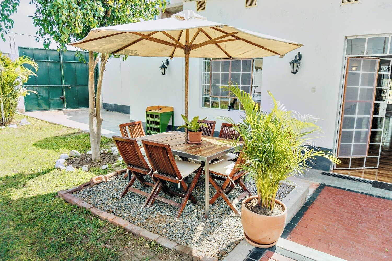 Une terrasse extérieure avec une table et des chaises en bois, un grand parasol et des plantes en pot.