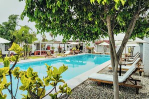 A swimming pool with lounge chairs and umbrellas, surrounded by greenery and buildings. - Beautiful country house in Chiclayo's Ferreñafe neighborhood with a 120-square-meter pool and 5 bedrooms (Lambayeque)