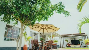 Un patio con mesa y sillas, un paraguas grande y una zona de barbacoa.