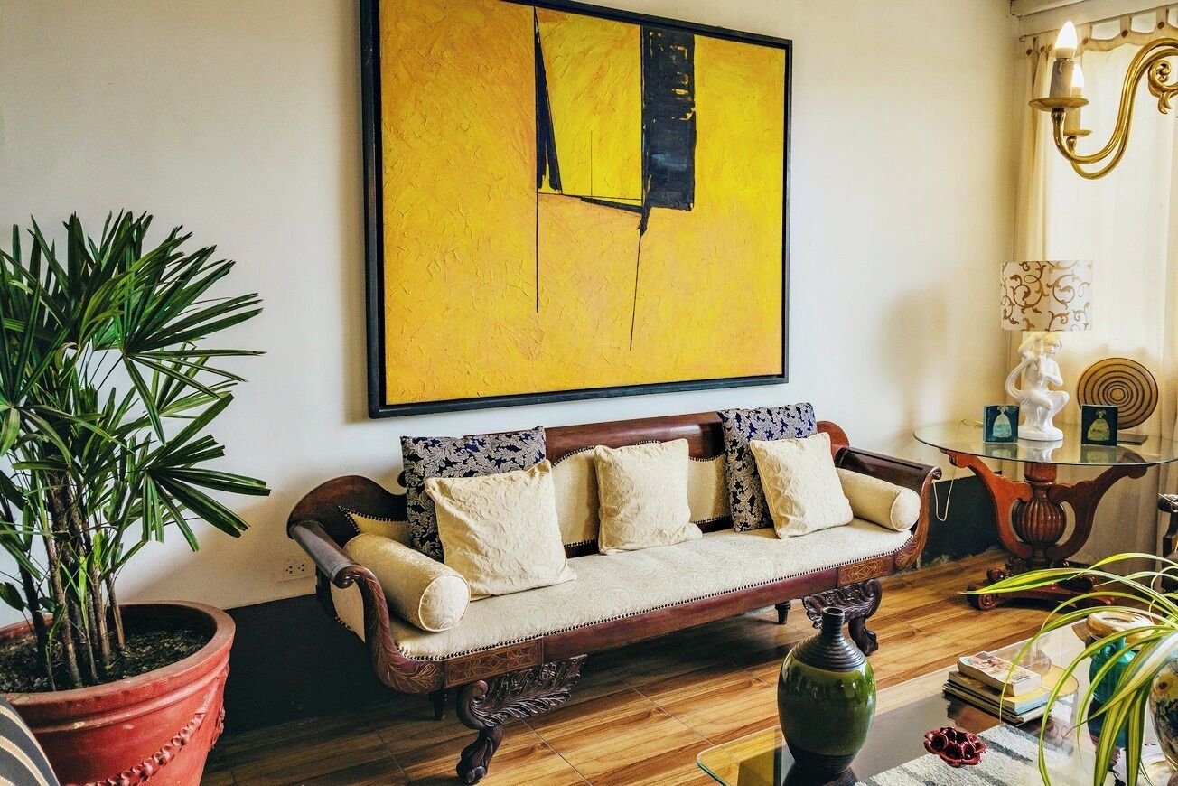 A cozy living room with a vintage sofa, a large abstract painting, and a potted plant.