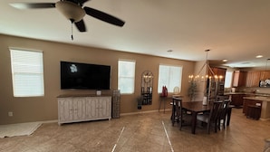A spacious living area with a flat-screen TV, a ceiling fan, a dining table with chairs, and a kitchen area with wooden cabinets and a built-in island. - Dove Mountain Perserve, gated, dog friendly home. (Marana)