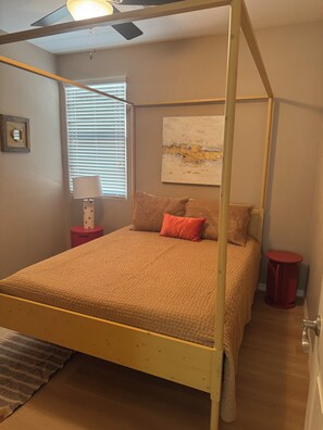 A bedroom with a four-poster bed, a bedside table, a lamp, and a painting on the wall.