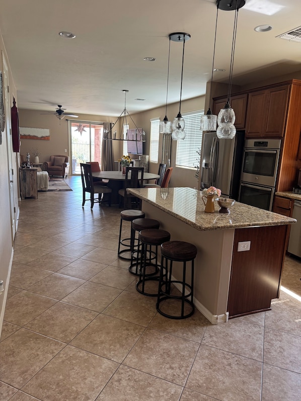A spacious kitchen with a central island, bar stools, and modern appliances. - Dove Mountain Perserve, gated, dog friendly home. (Marana)