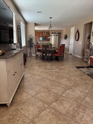 A spacious kitchen with a dining area, featuring a central island, a chandelier, and a large window with blinds. - Dove Mountain Perserve, gated, dog friendly home. (Marana)