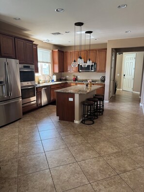 A modern kitchen with granite countertops, stainless steel appliances, wooden cabinets, and pendant lighting.