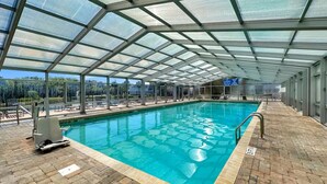 An indoor swimming pool with a glass ceiling, tiled floor, and a lifeguard chair.