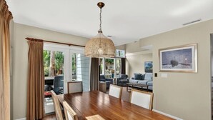A spacious living room with a wooden dining table, a large woven chandelier, and a view of the outdoors.