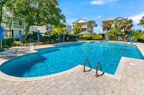 A swimming pool with a brick deck, lounge chairs, and umbrellas.