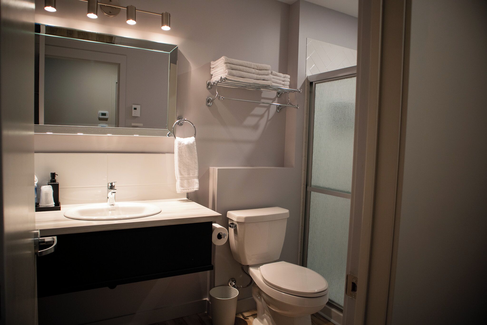 A modern bathroom with a sink, mirror, towel rack, toilet, and a trash bin.